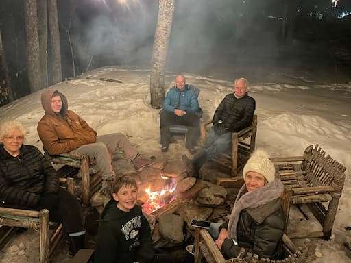 A group of people gathered around a campfire, sharing stories and enjoying the warmth of the flames in a nighttime setting.