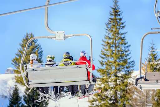 Ski lift carrying several skiers up a mountain on a sunny winter day at a resort.